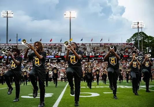Mighty Marching Hornets trumpet players high-step in black and gold A shirts before a packed stadium